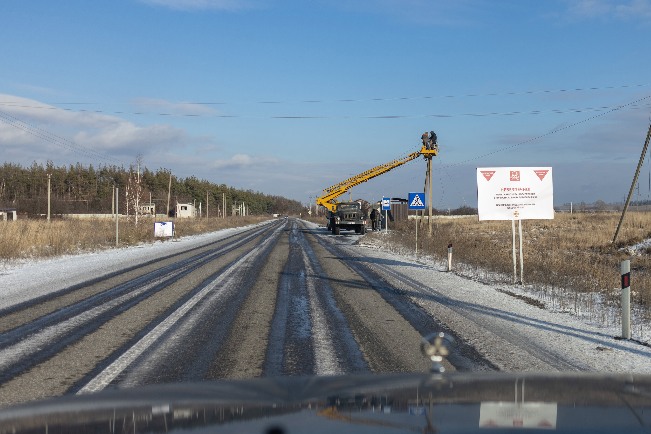 Дорогою до села ремонтують лінії електропередач. Встановлена табличка з попередженням про міни у полях та лісах.
