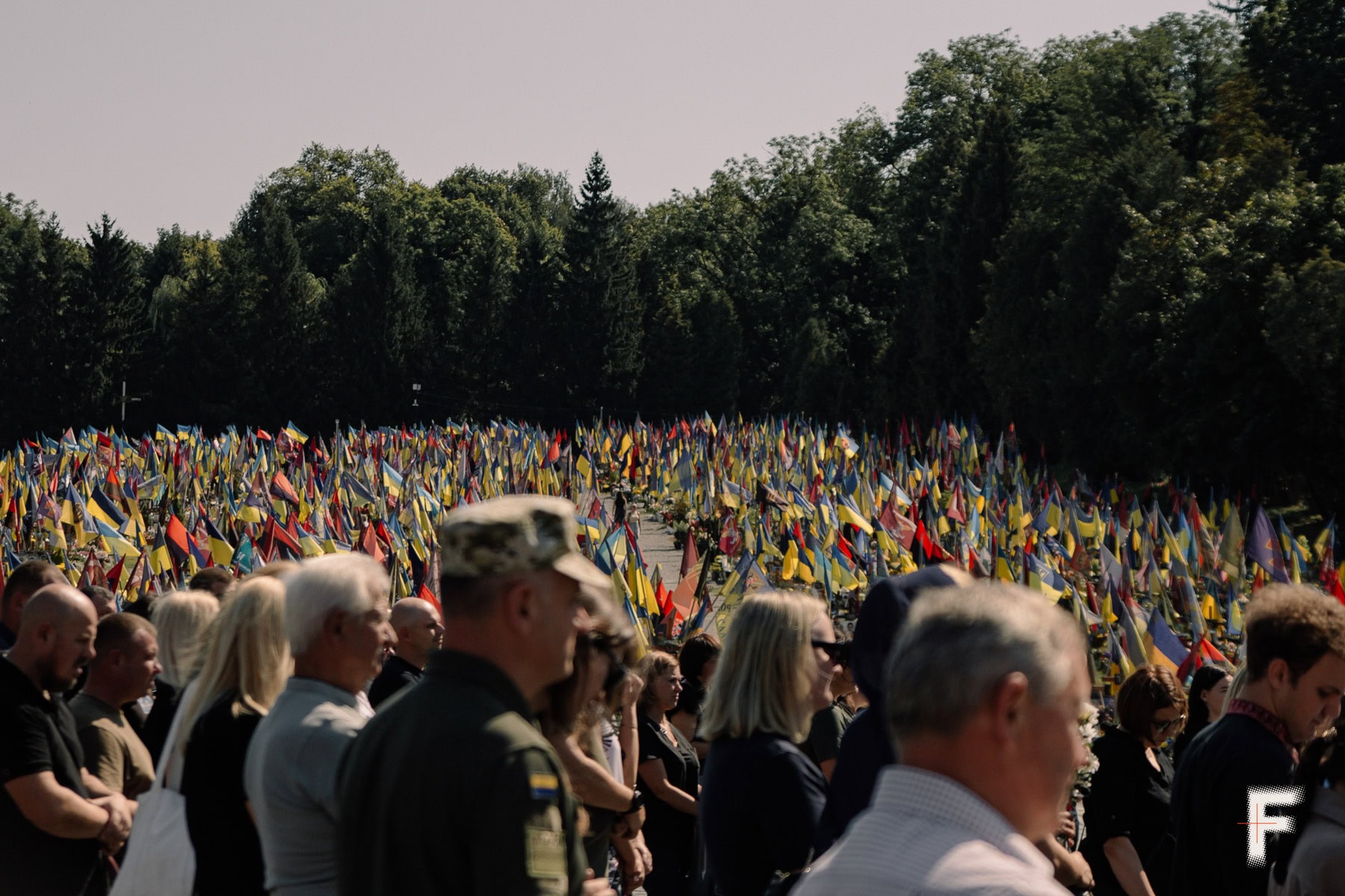 Люди на кладовищі, на задньому плані майорять українські прапори