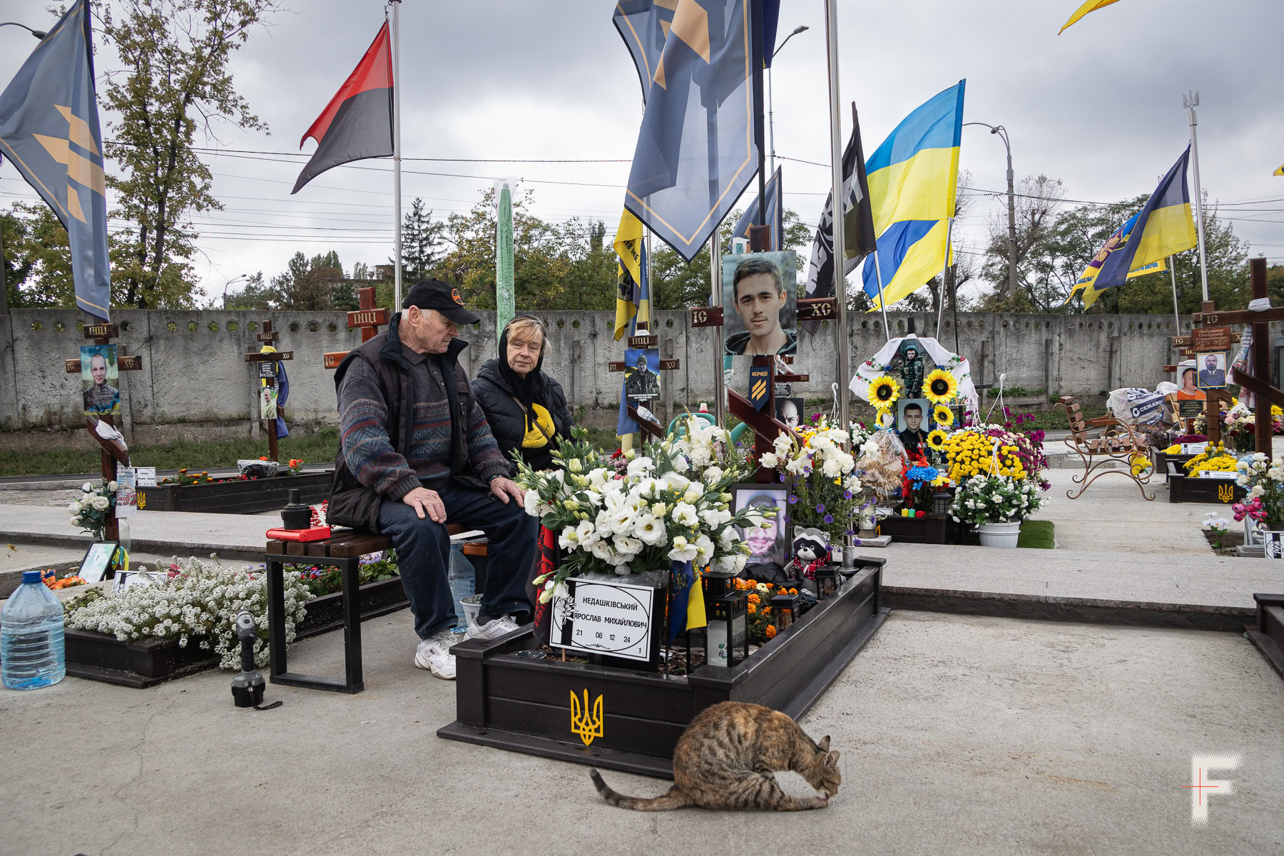Могила молодого загиблого військового, на лавці сидять літні люди