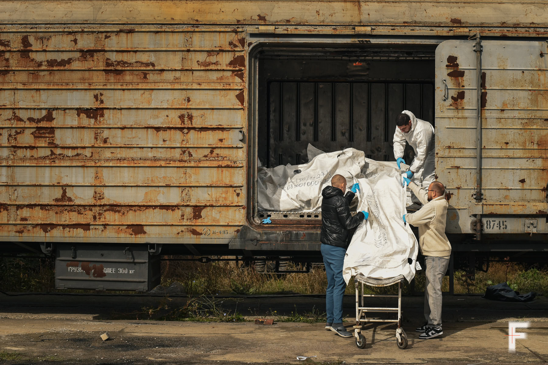 Троє чоловіків завантажують білий пакет до старого залізничного вагона.