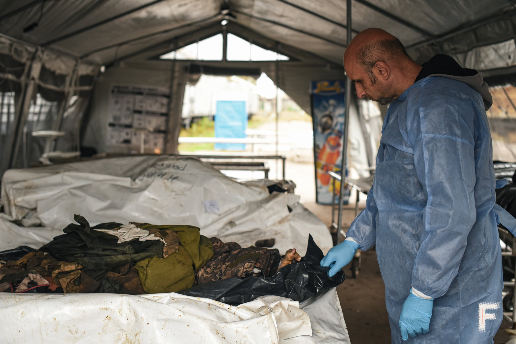 Чоловік у синій сорочці дивиться на тіло загиблого військового.