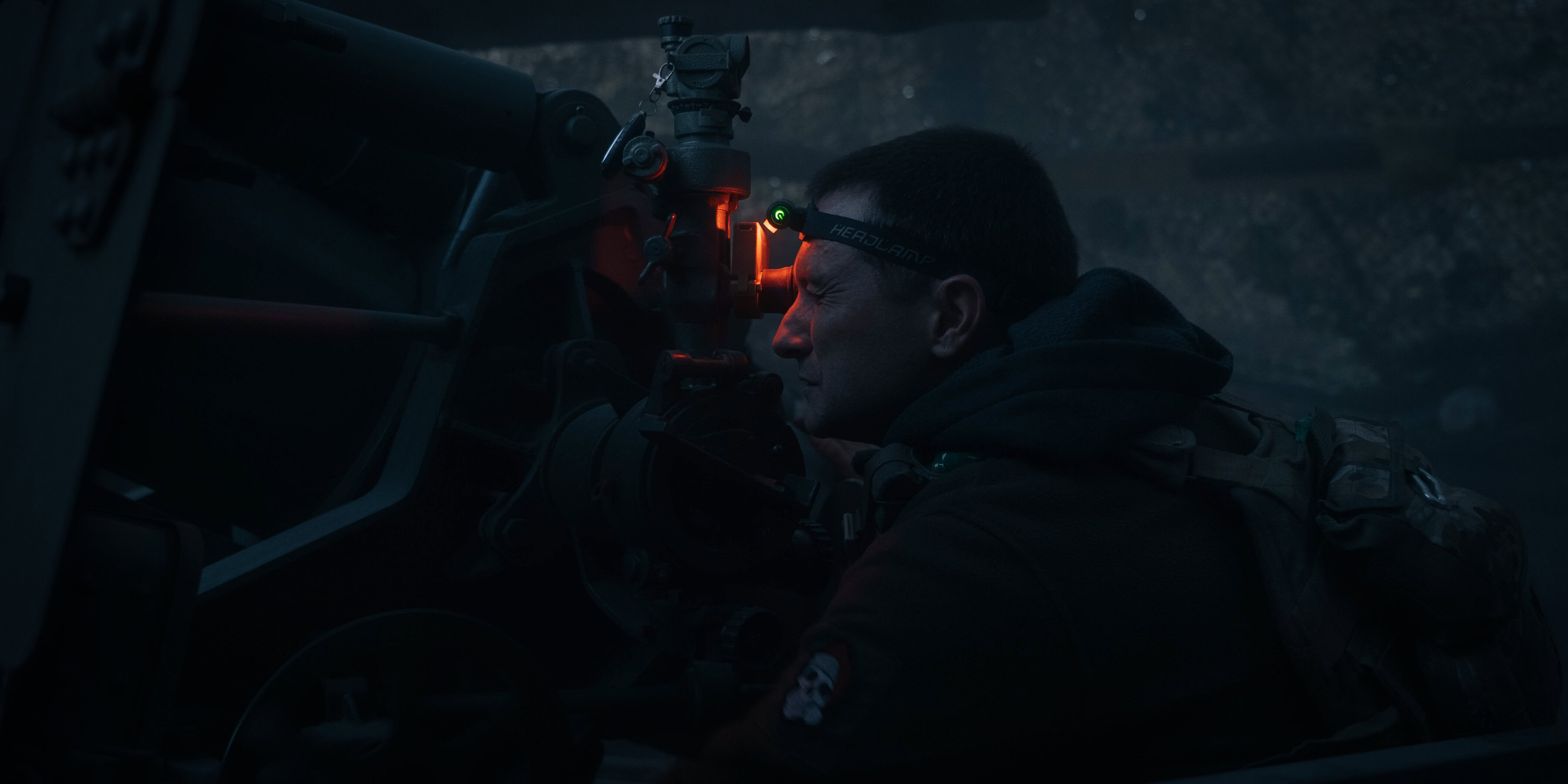 Український військовий спостерігає за позиціями ворога через приціл артилерійської установки.