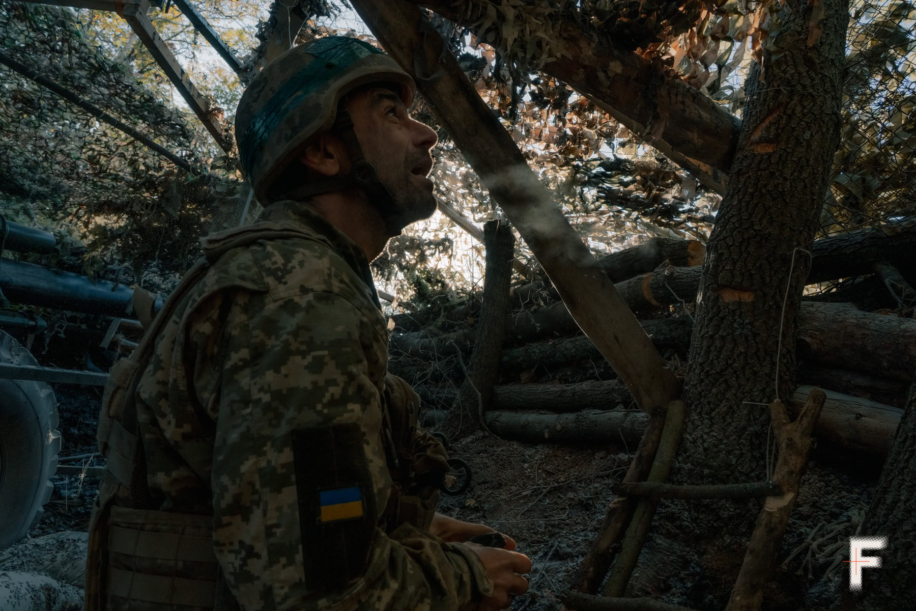 Український боєць відпочиває на позиції, схованій під камуфляжною сіткою.