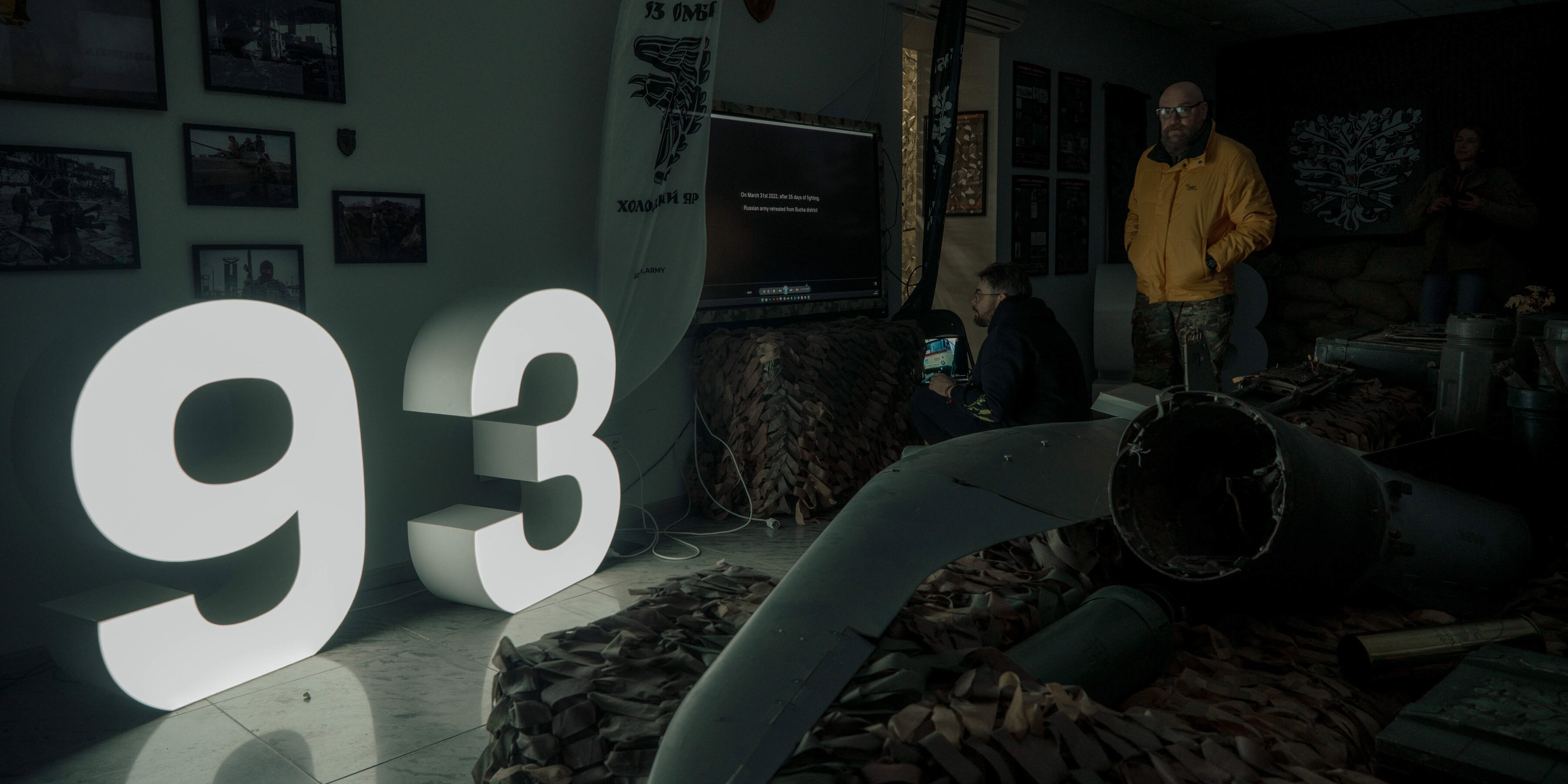 Чоловік у жовтій куртці стоїть у кімнаті поруч із розбитим ворожим дроном.