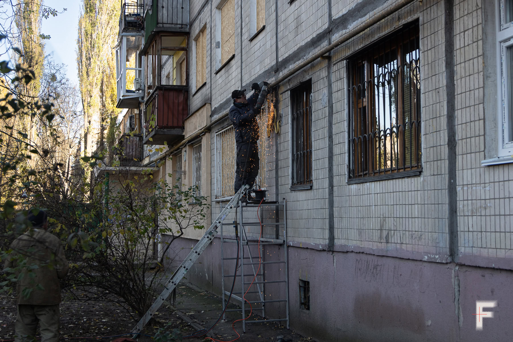 Чоловік працює на драбині, ремонтує труби в пошкодженій будівлі.