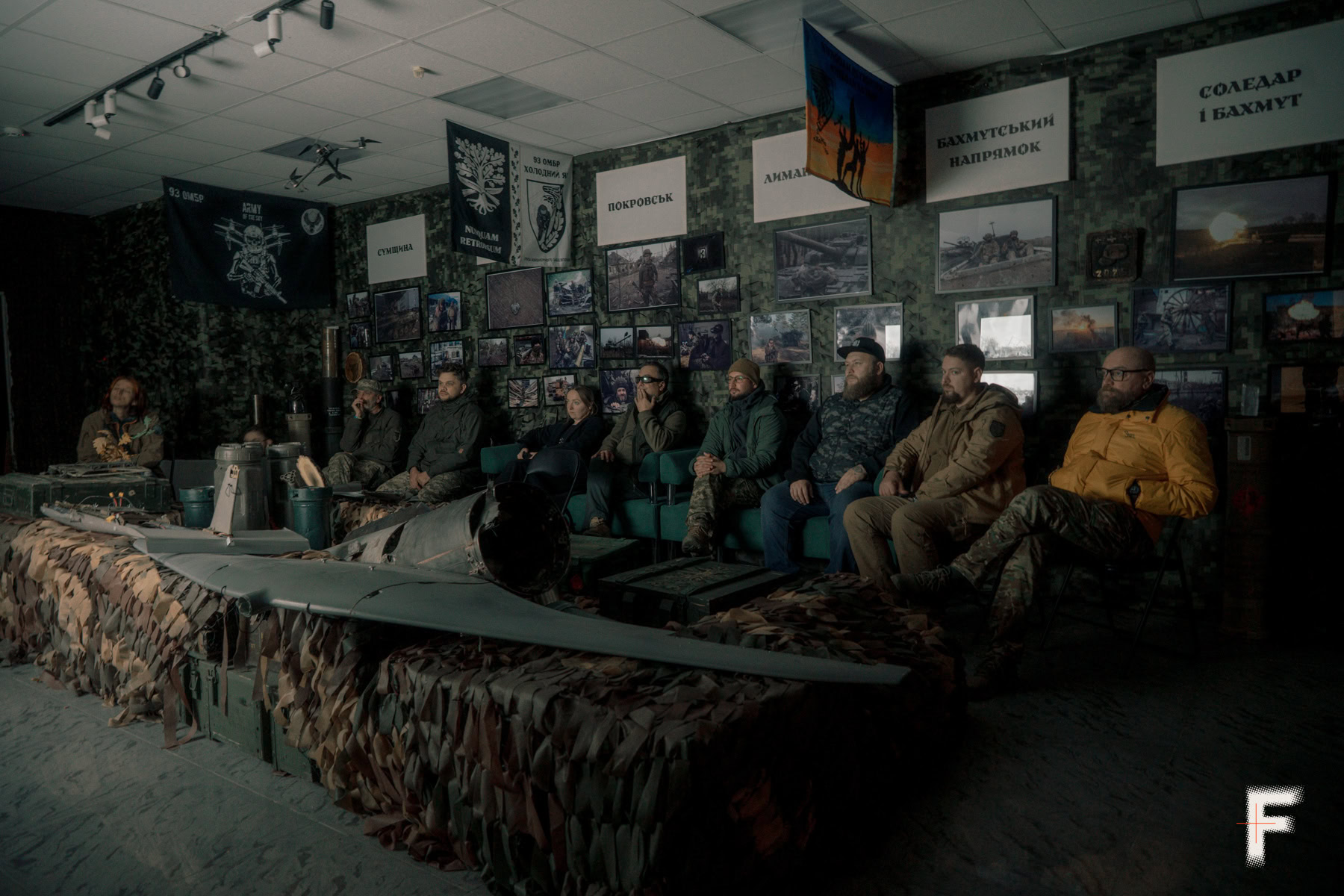 Група людей у кімнаті оглядає розбитий дрон, виставлений як трофей.