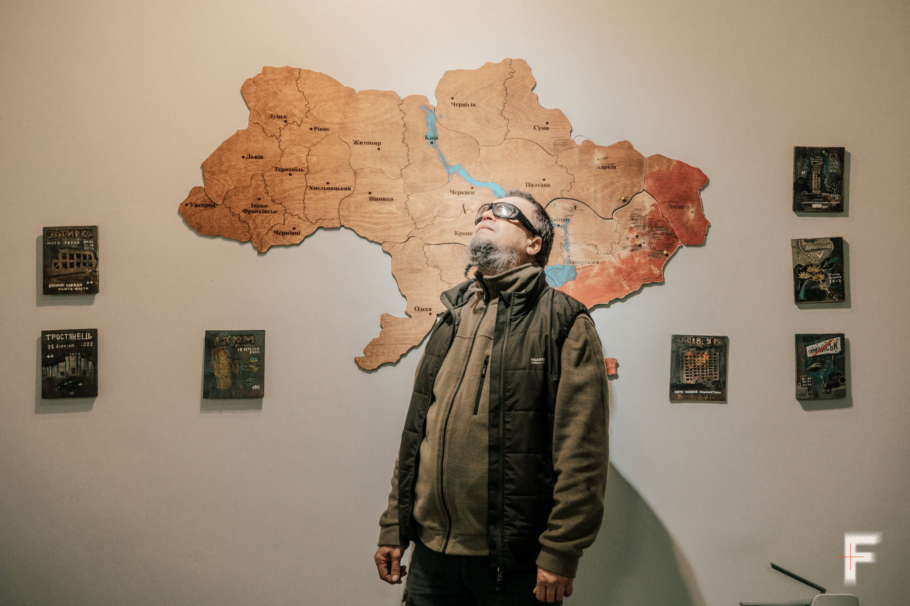 Чоловік стоїть перед дерев’яною картою України та вдивляється вгору.