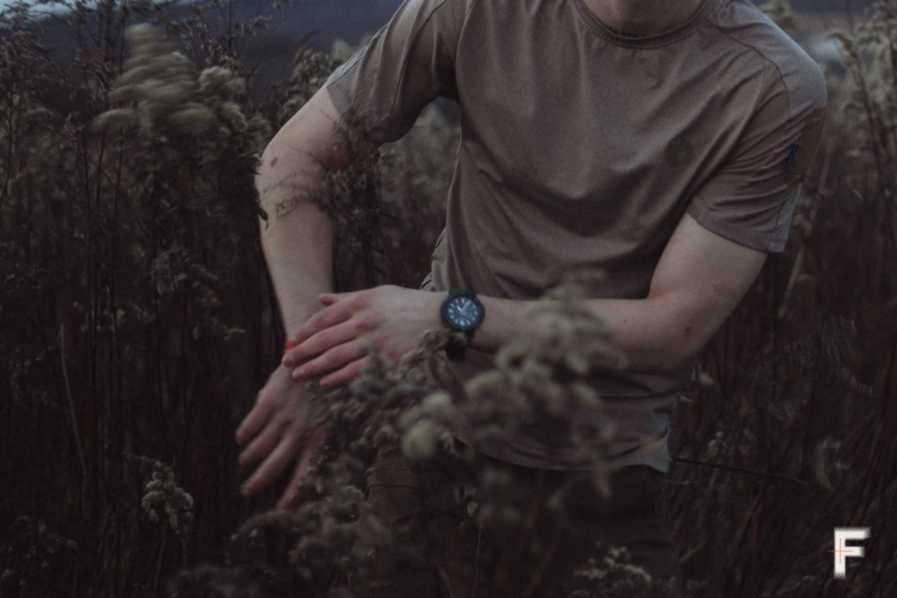 Молодий чоловік стоїть серед польової рослинності, на зап’ясті видно наручний годинник
