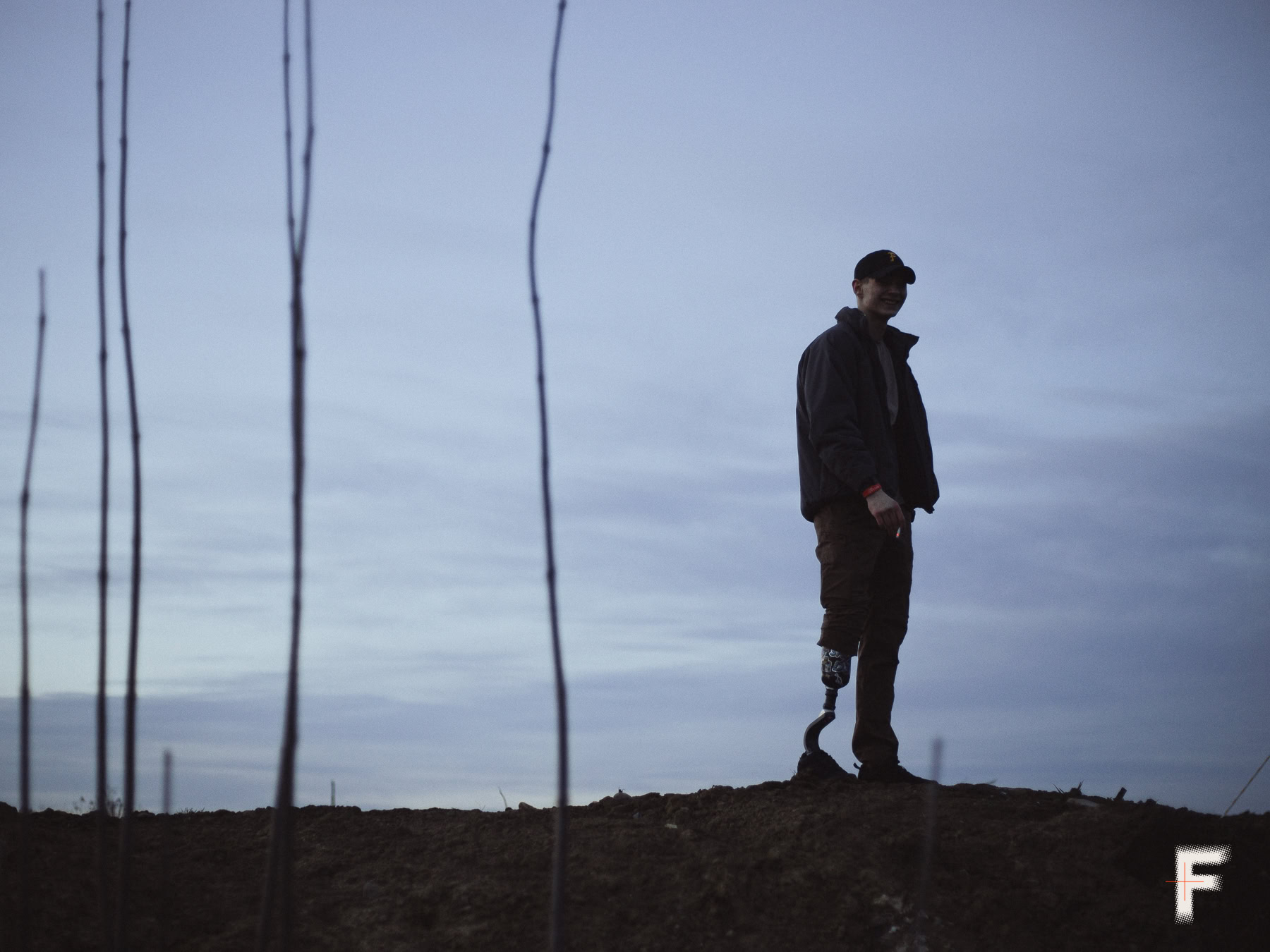 Молодий чоловік з протезом ноги стоїть на відкритій ділянці землі