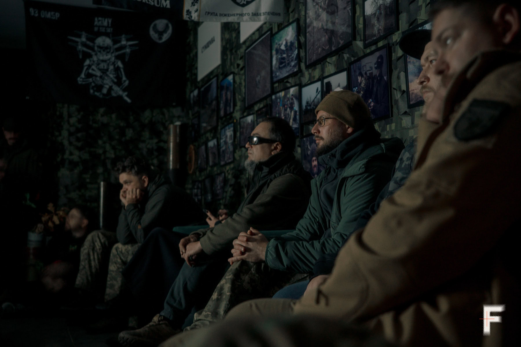 Військовослужбовці в цивільному одязі сидять у кімнаті з фотографіями та дивляться на великий екран.