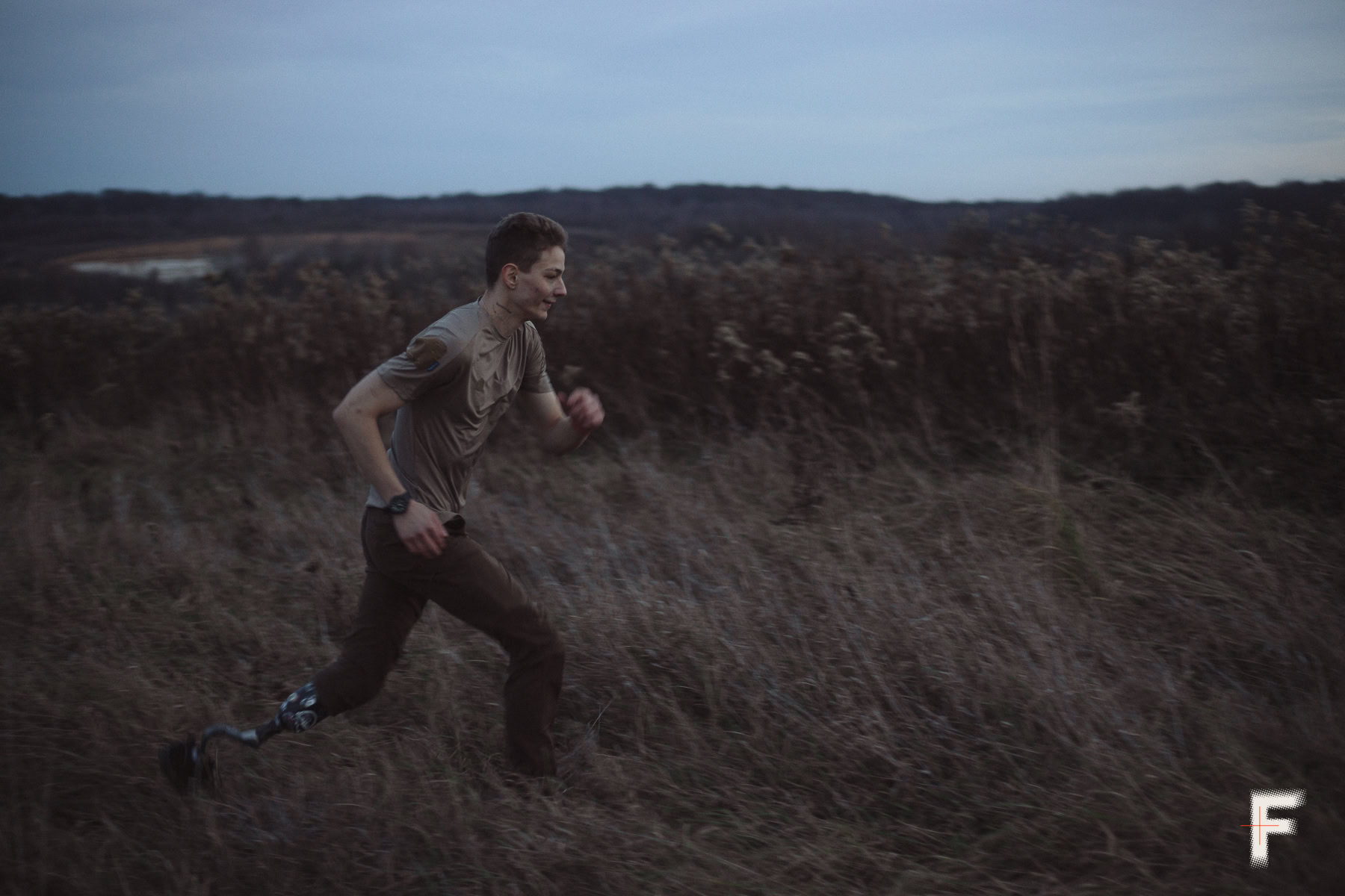 Молодий чоловік із протезом ноги біжить через поле на відкритій місцевості