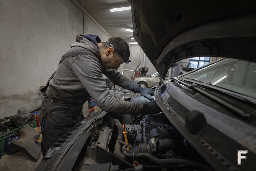 Механік ремонтує автомобіль у гаражі, працюючи під відкритим капотом.
