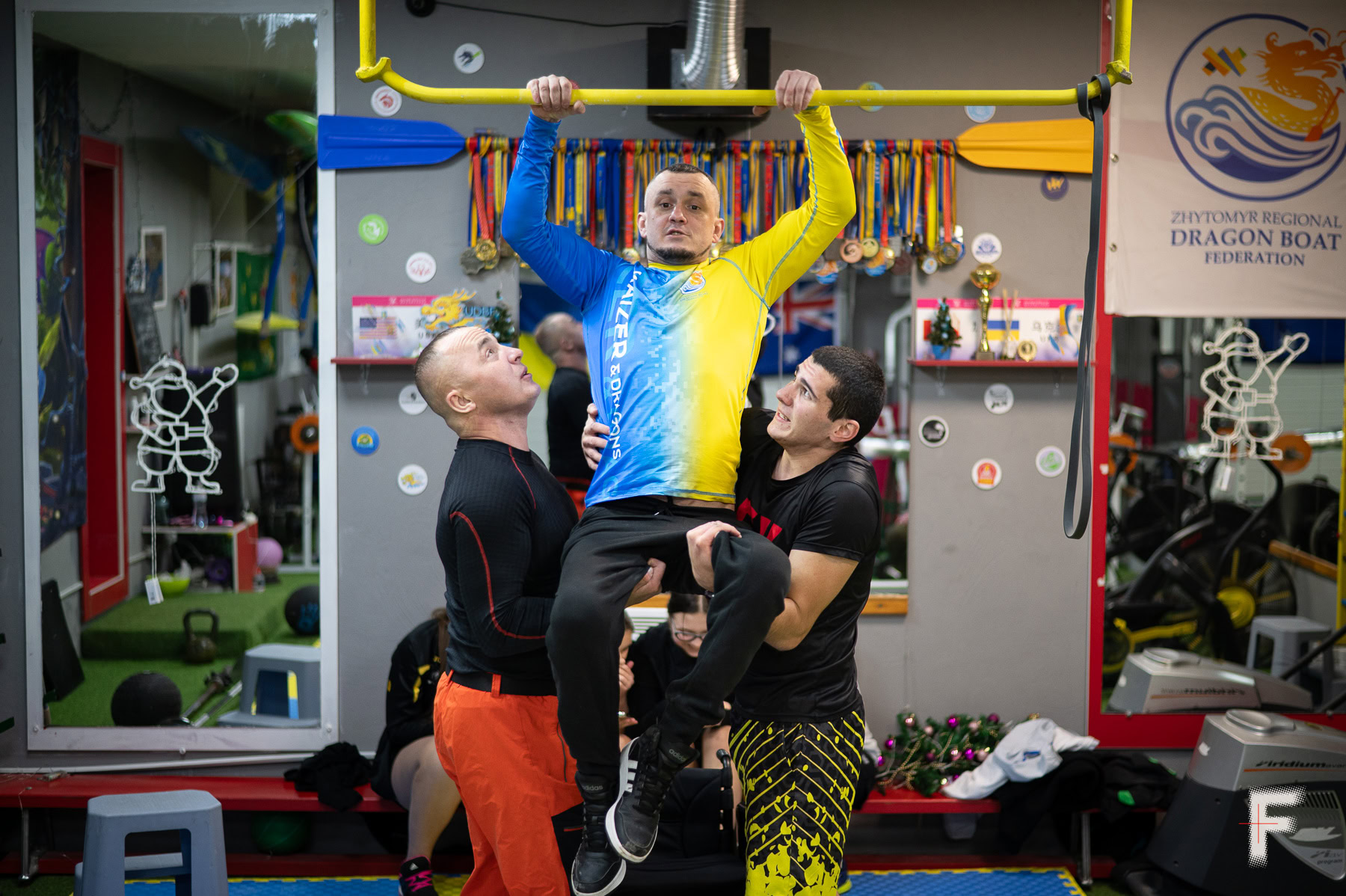 Тренер допомагає Івану підтягнутися на турніку в спортивному залі.