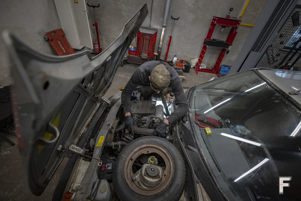 Механік працює під капотом автомобіля, виконуючи ремонтні роботи в гаражі.