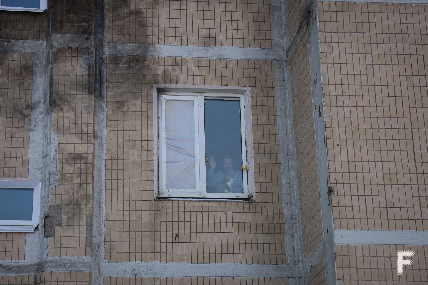 Наталія Зайченко стоїть біля вікна та гладить кота під час масових відключень світла на Троєщині в Києві.