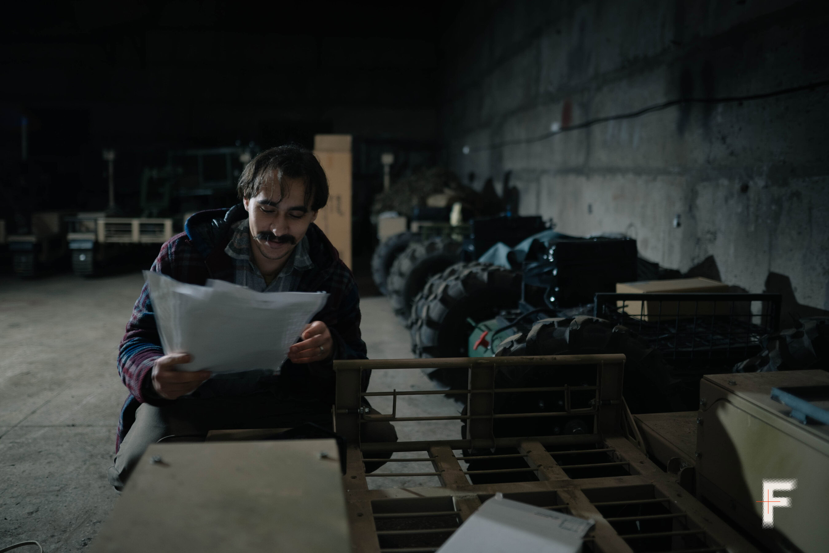 Людина сидить у ангарі на фоні наземних військових дронів, підготовлених до тестування або ремонту.