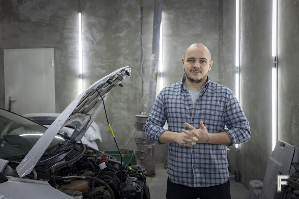 Портрет чоловіка, який стоїть біля автомобіля з відкритим капотом після ремонту.