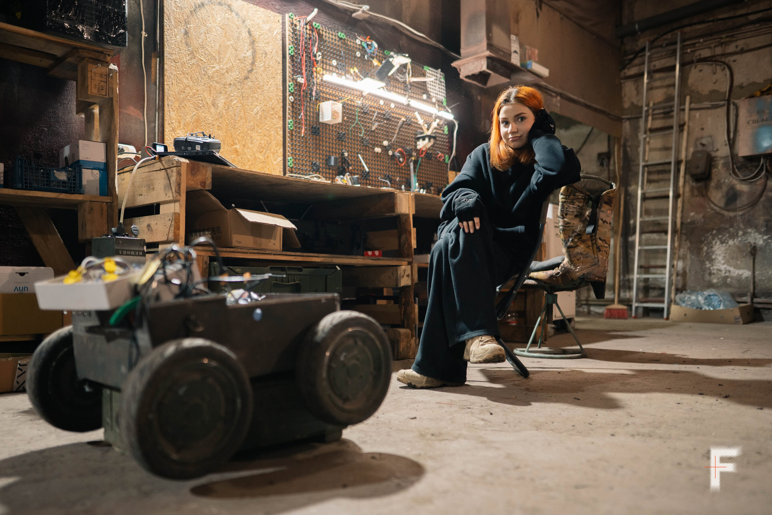 Жінка з помаранчевим волоссям сидить у виробничому ангарі, де збирають і тестують наземні роботизовані системи.