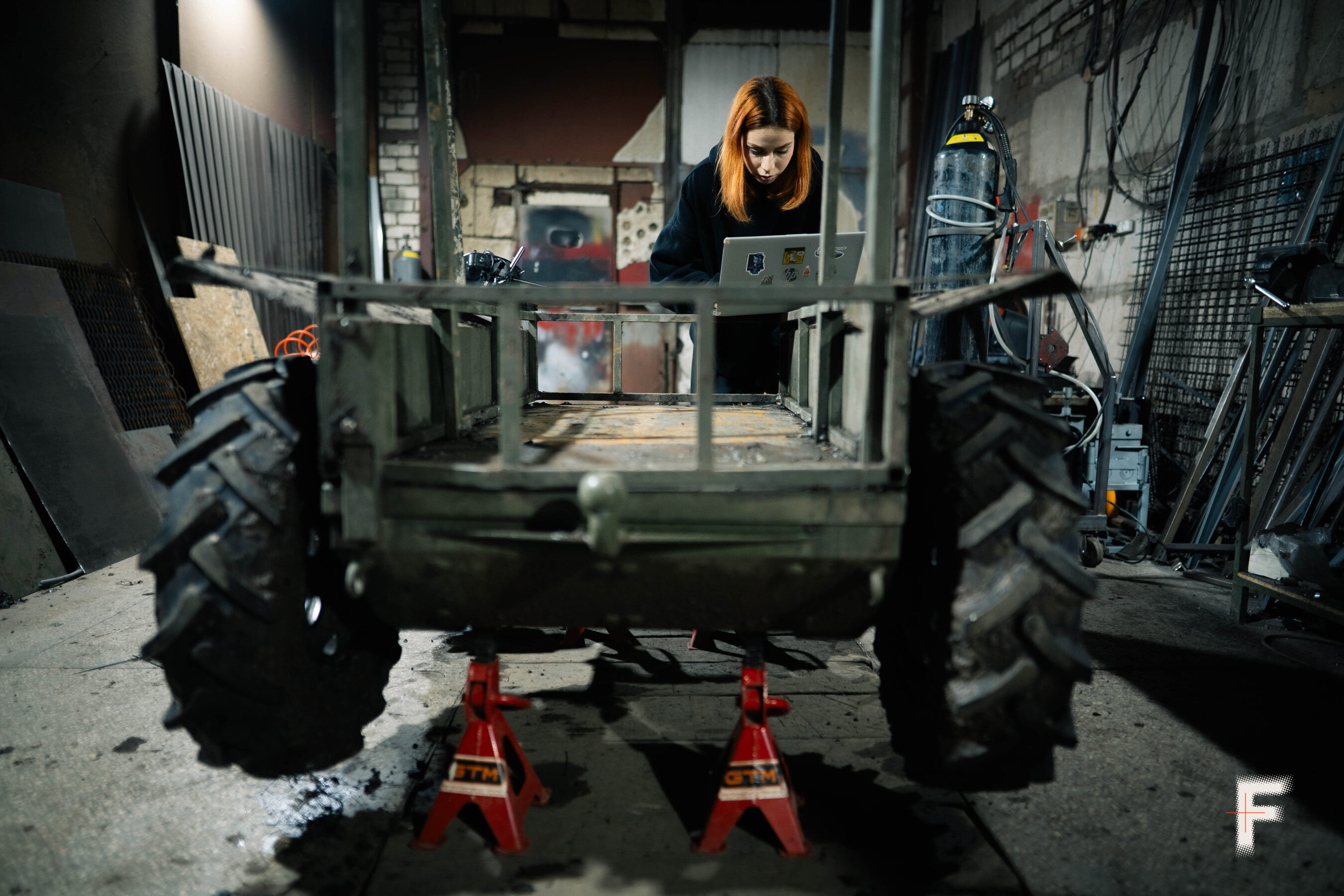 Жінка з помаранчевим волоссям працює за комп’ютером під час тестування наземного військового робота в ангарі.
