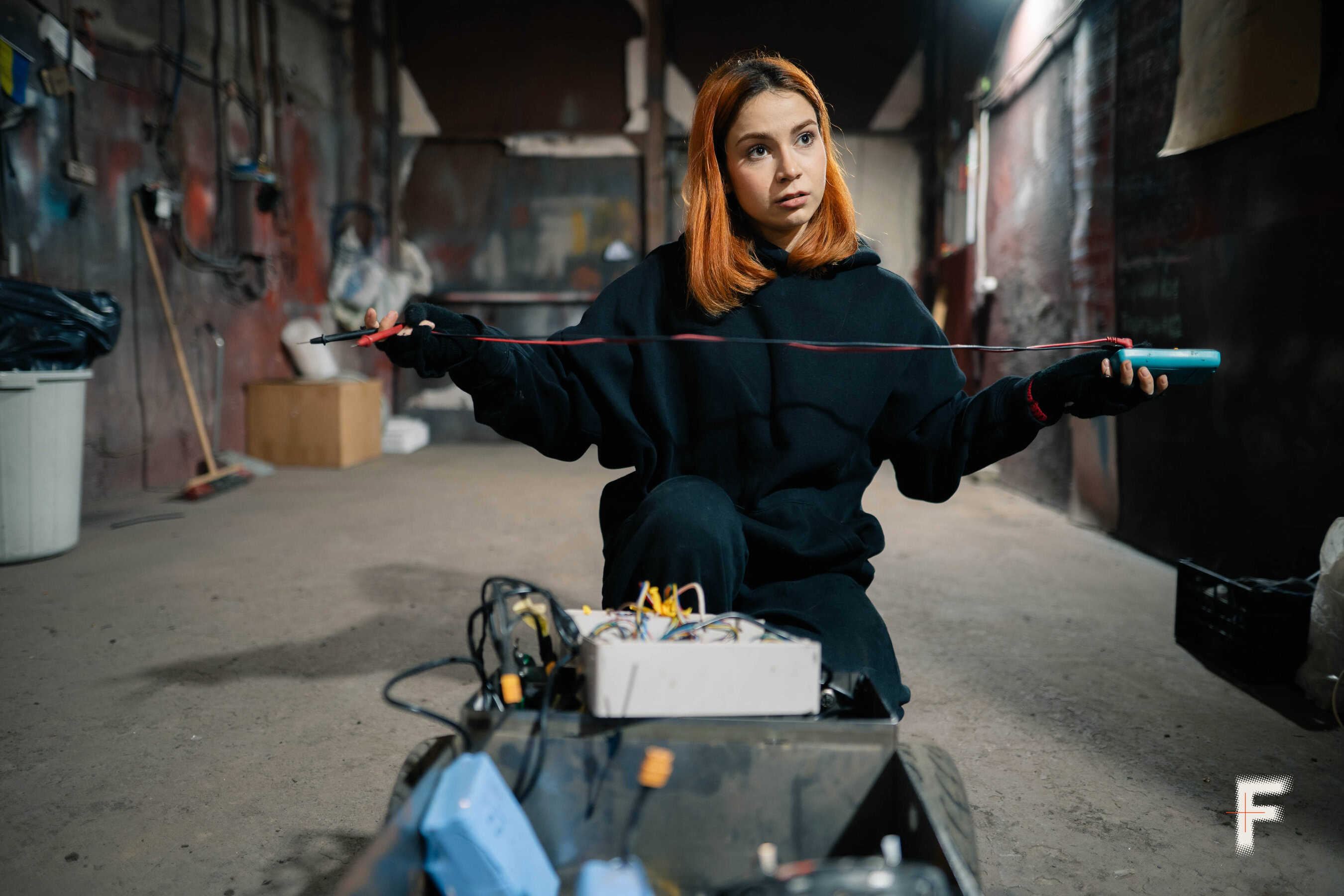 Жінка тримає електронний пристрій з червоним і чорним проводами — компонент для військової роботизованої техніки.