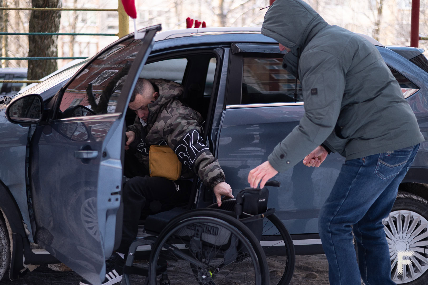 Сусід допомагає Івану пересісти з автомобіля на крісло.