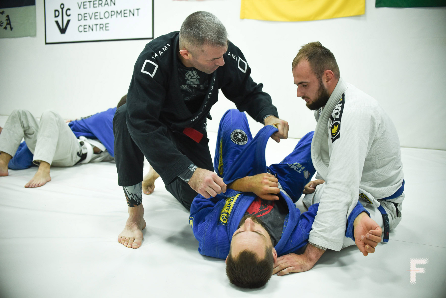 Троє чоловіків тренуються з джиу-джитсу на татамі в межах реабілітаційної програми для ветеранів.