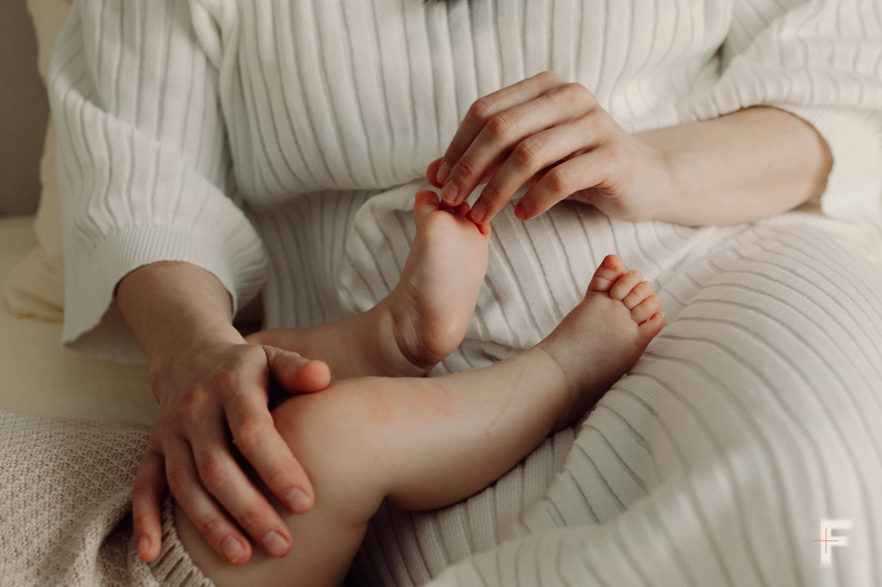 Крупний план рук матері, яка ніжно торкається пухких ніжок немовляти.