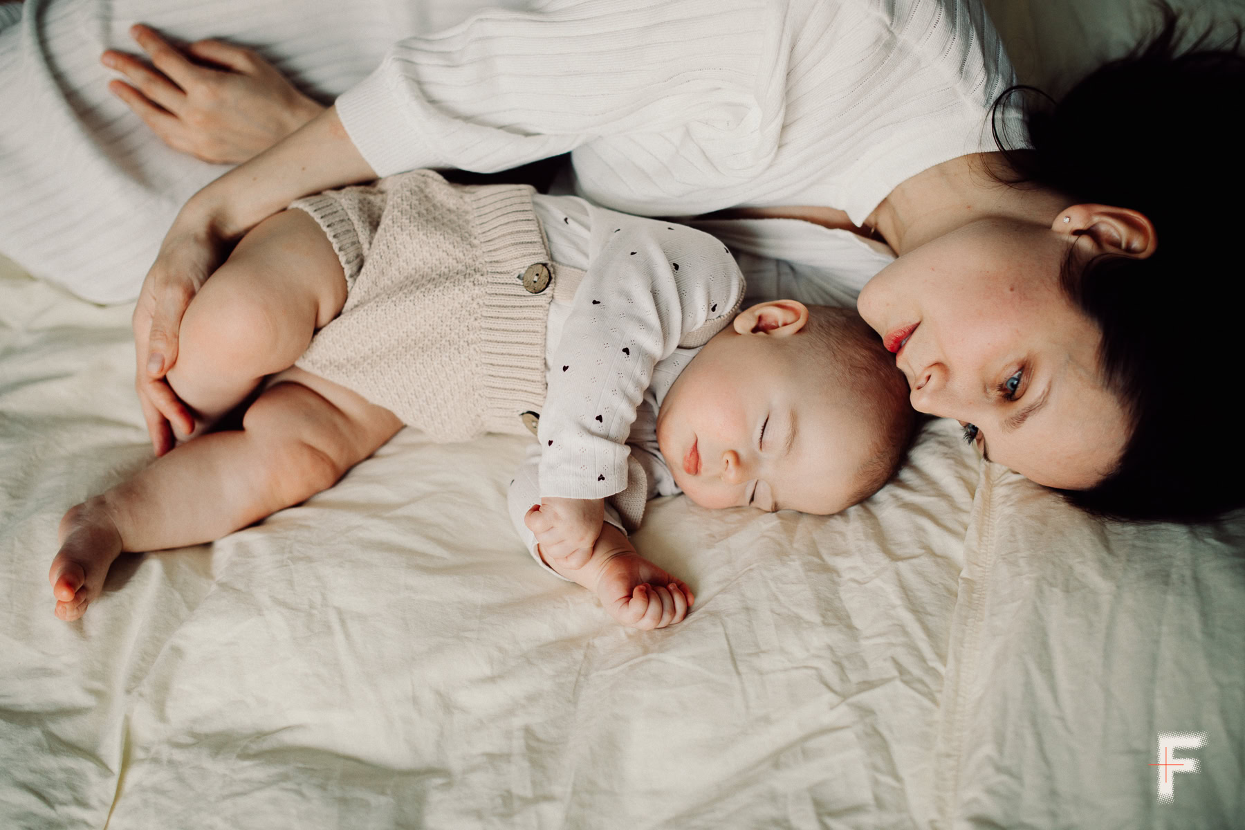 Мати лежить у ліжку поруч із немовлям, намагаючись його приспати.