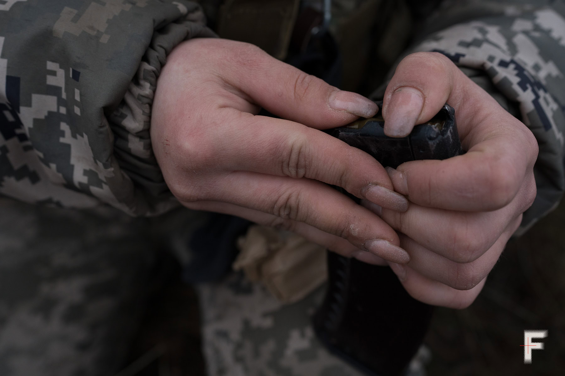 Крупний план рук колишньої ув’язненої, яка заряджає магазин зброї.