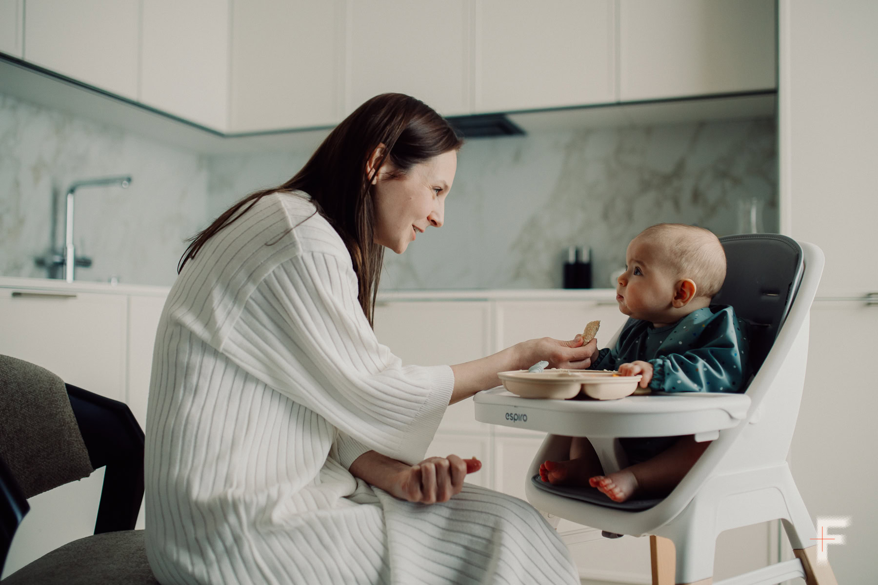 Мати годує немовля, яке сидить у дитячому стільчику для годування.