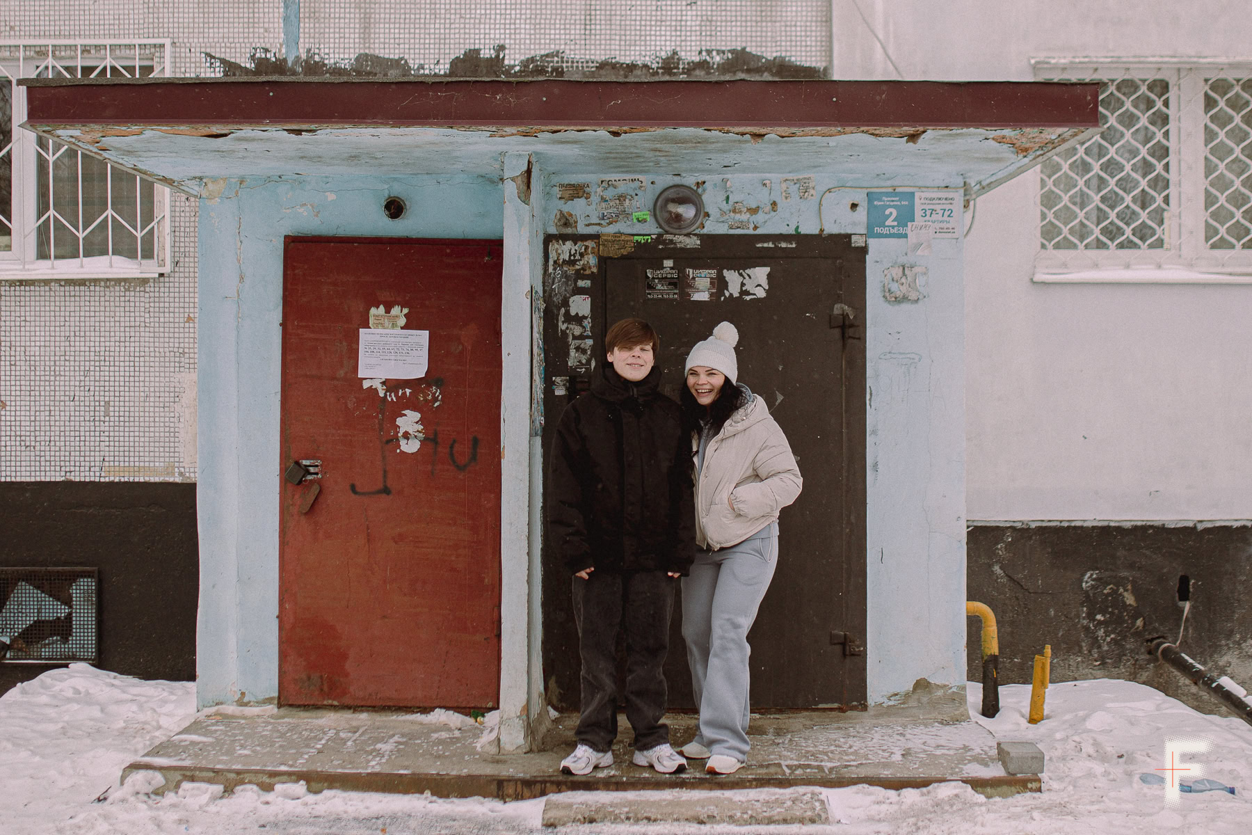 Жінка та підліток стоять біля входу до багатоповерхового будинку.