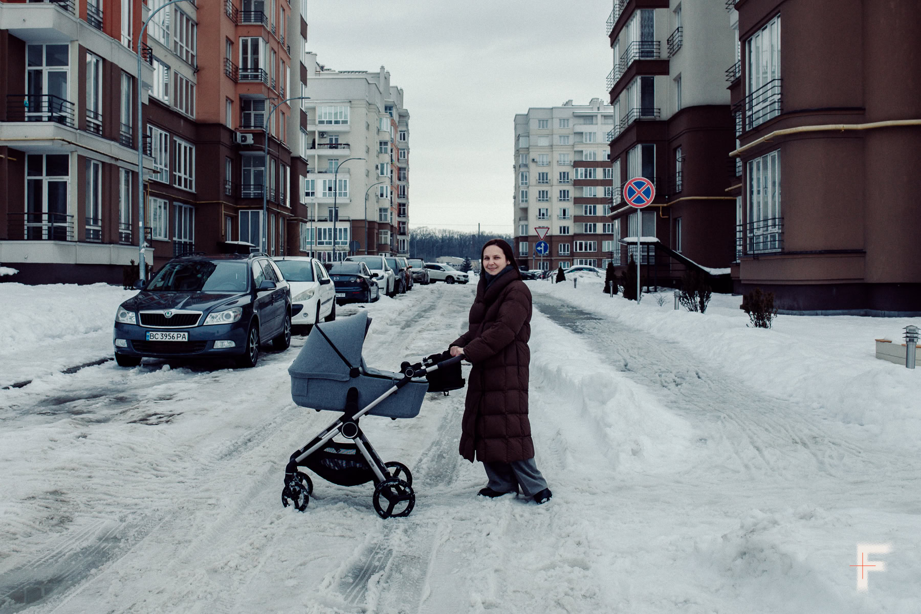 Жінка штовхає дитячий візок із немовлям засніженою вулицею.