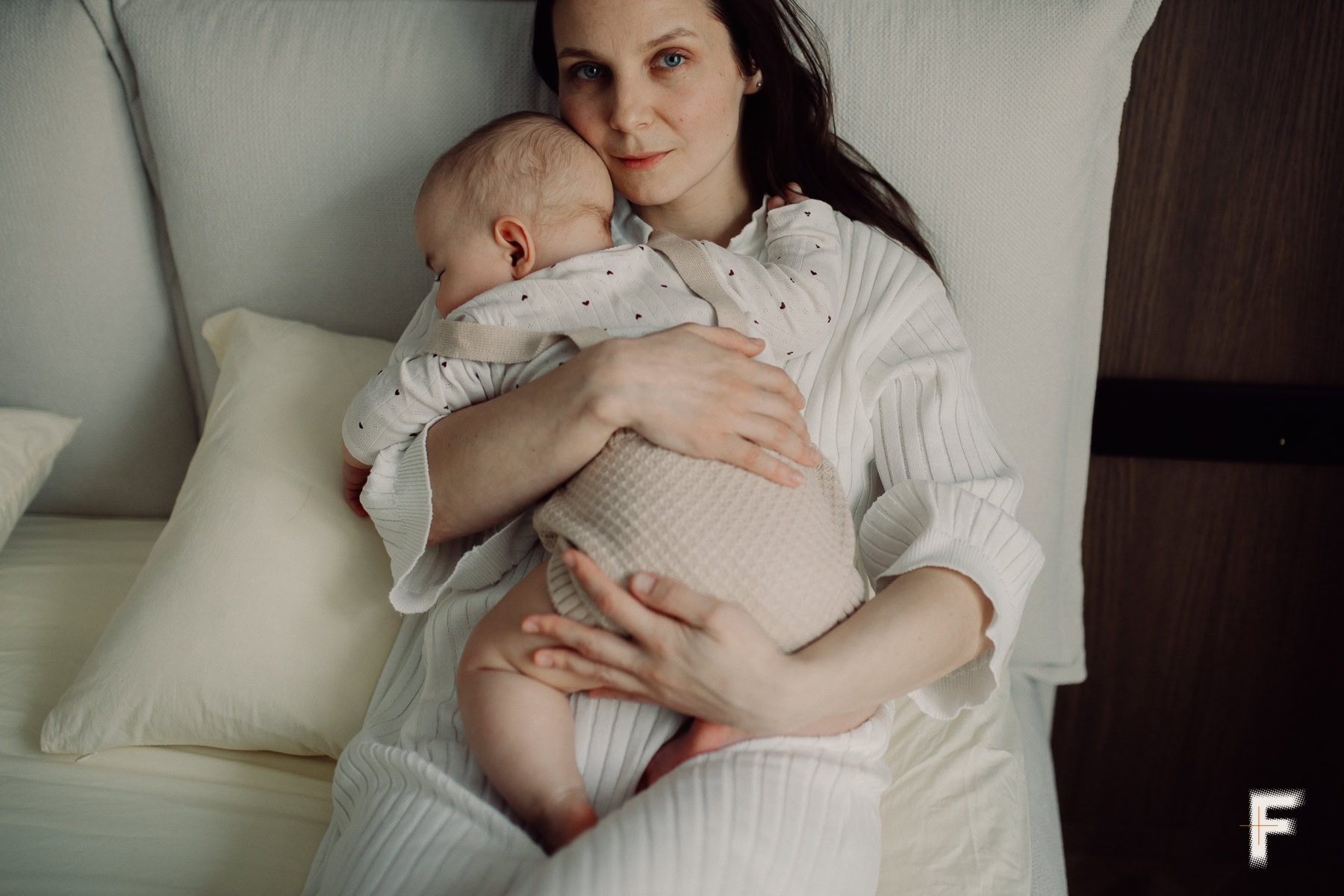 Мати сидить на ліжку та заколисує дитину на руках.