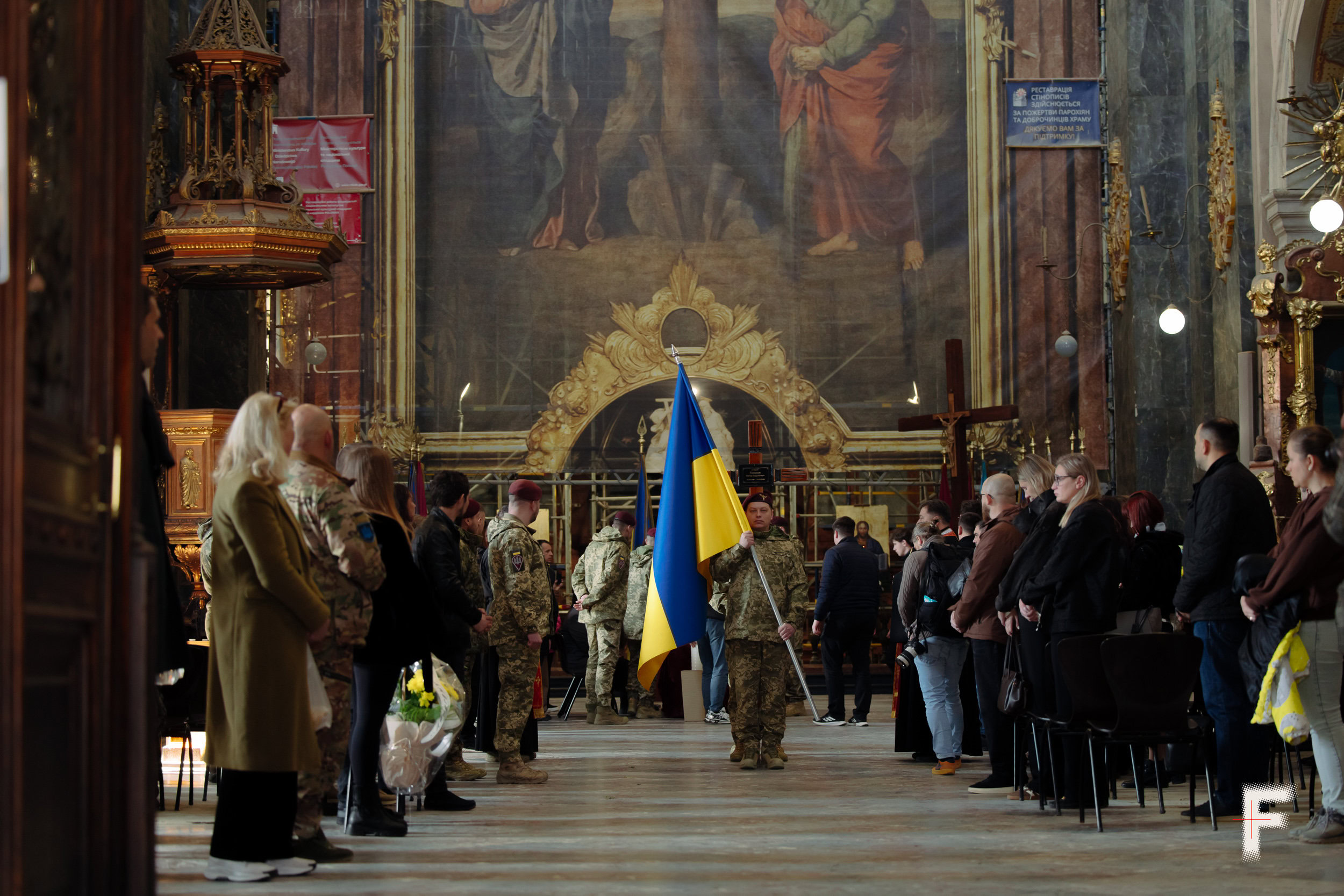 Український військовий тримає великий прапор біля церкви під час похорону