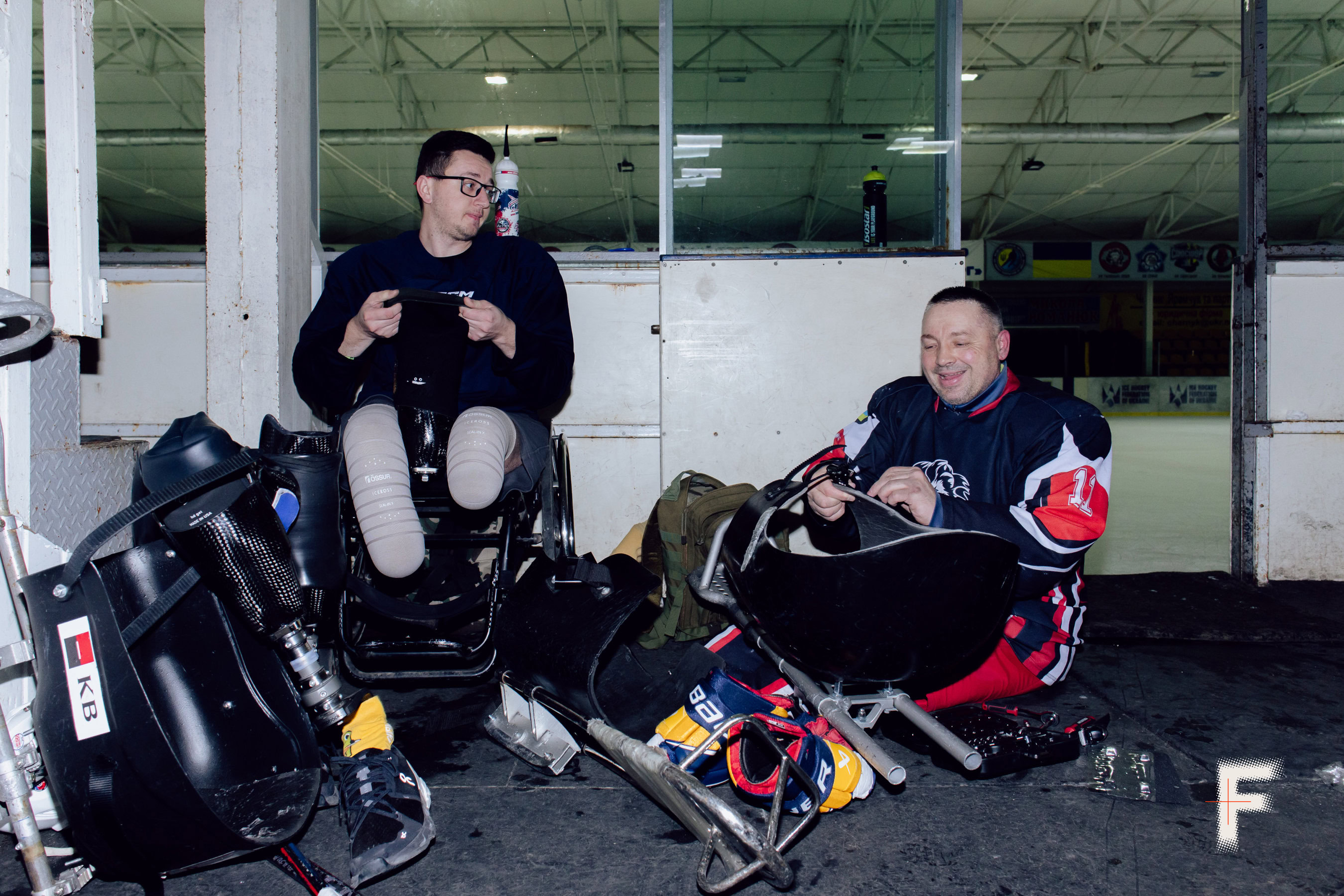 Двоє ветеранів з ампутаціями готуються до гри в хокей у роздягальні