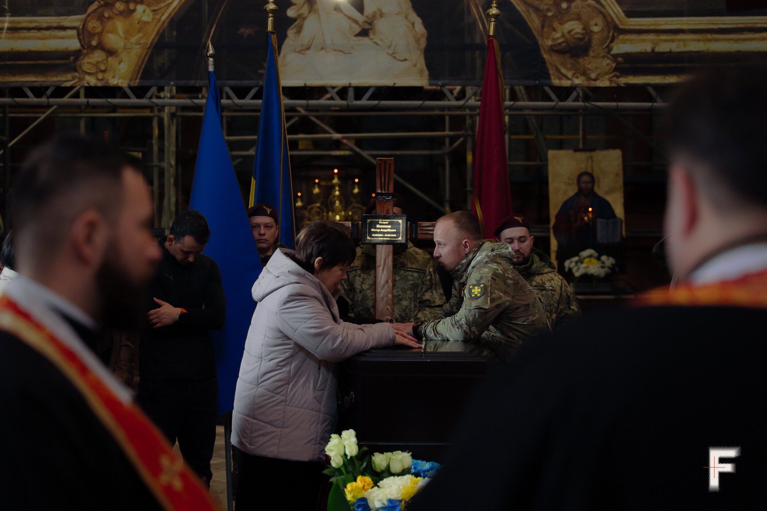 Жінка в зимовій куртці схилилася над труною свого загиблого сина