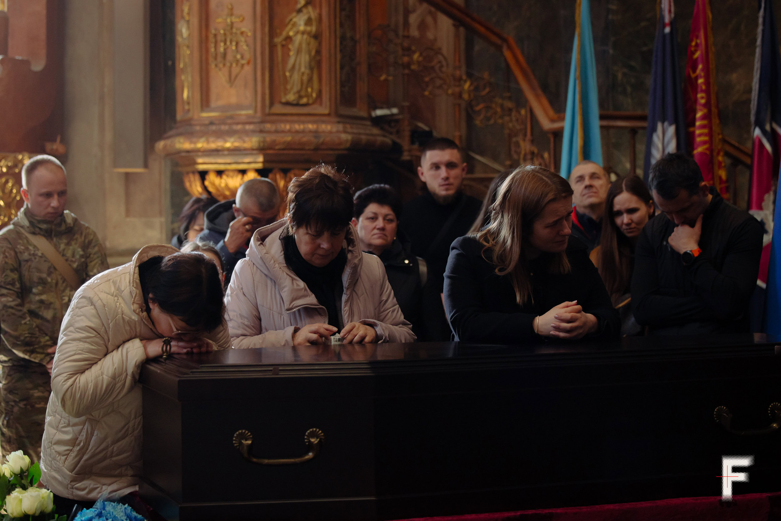 Три жінки стоять, спираючись на закриту труну під час прощання
