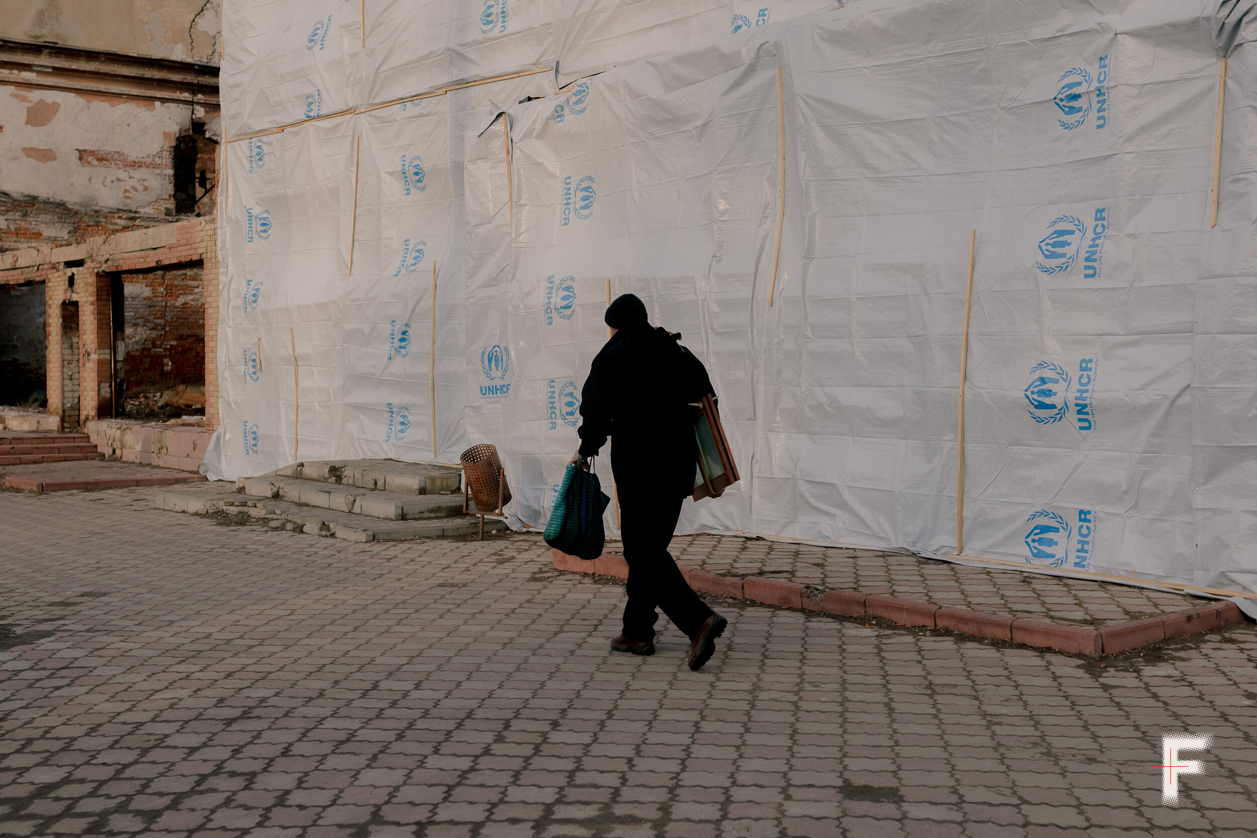 Чоловік іде вулицею повз банер агентства ООН у справах біженців UNHCR в Ізюмі