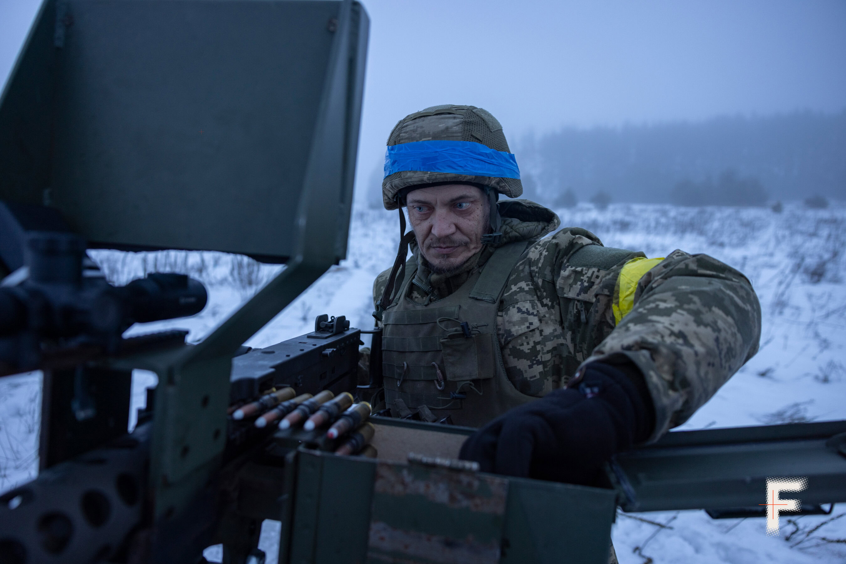 Командир мобільної вогневої групи у шоломі заряджає кулемет перед нічною роботою.