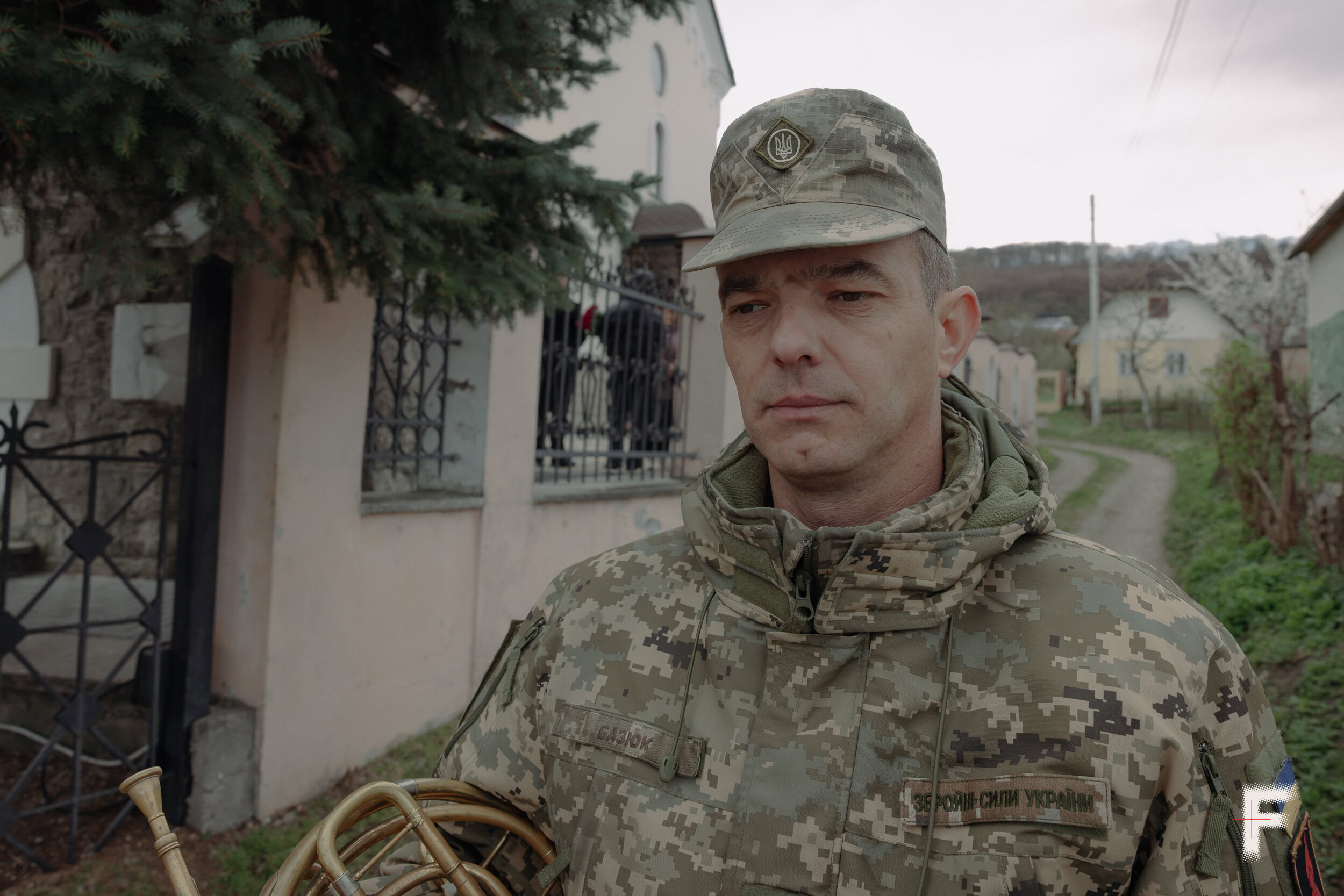 Військовий музикант Володимир Базюк тримає інструмент під час похоронної церемонії, Лисиничі, 2026