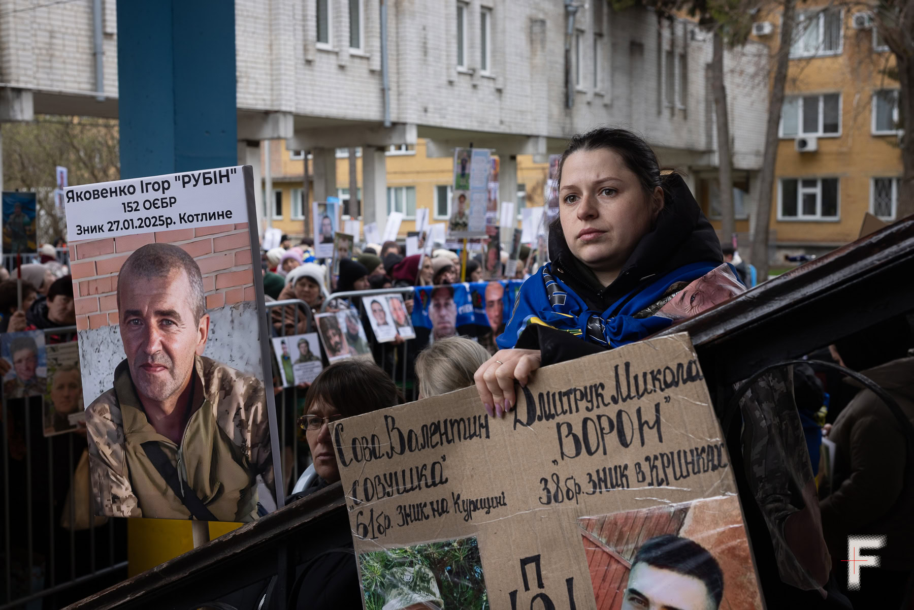 Жінка тримає плакати із зображеннями двох рідних, які перебувають у російському полоні, Україна, 2026
