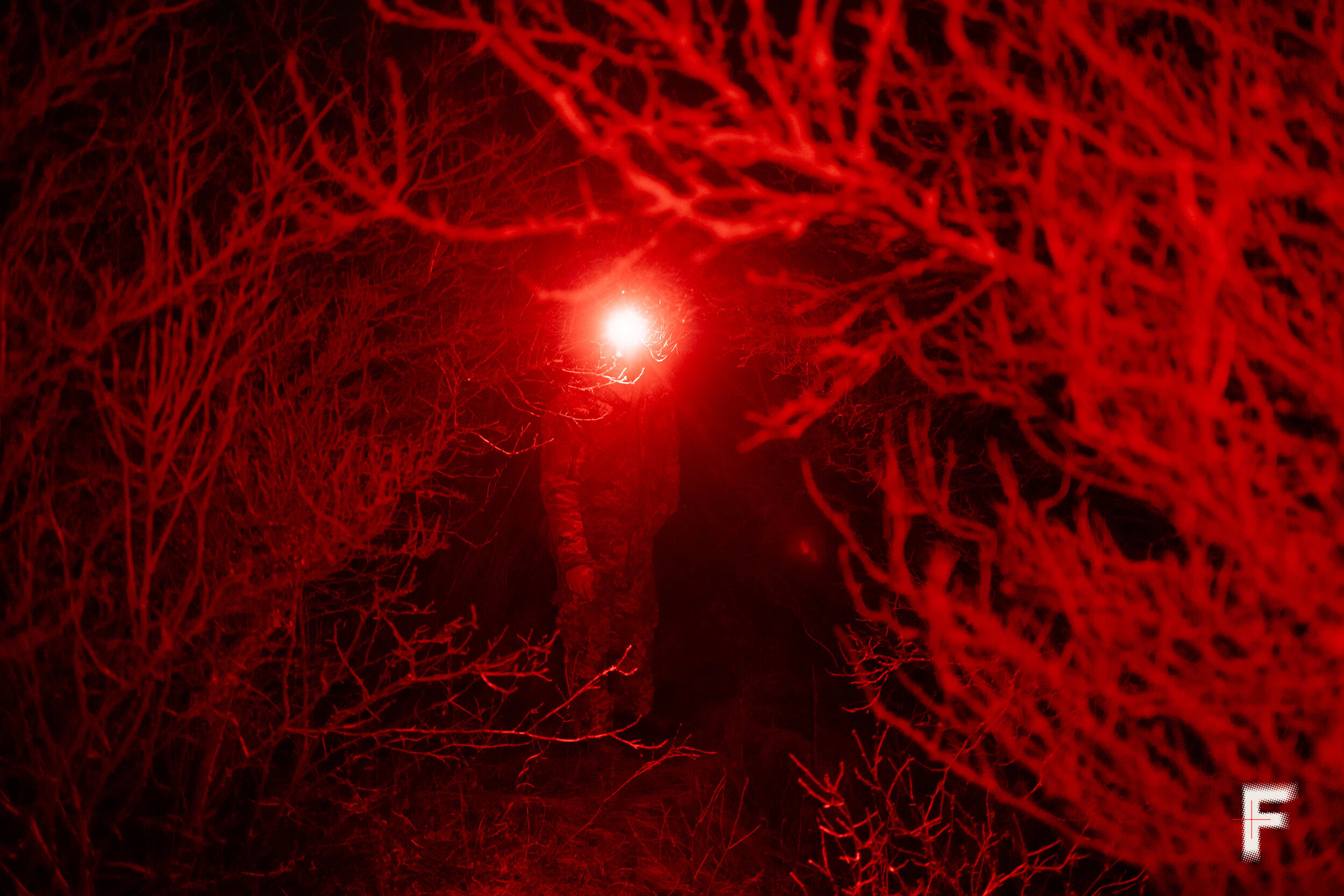 Український військовий рухається вночі крізь кущі, освітлюючи шлях яскравим червоним світлом.