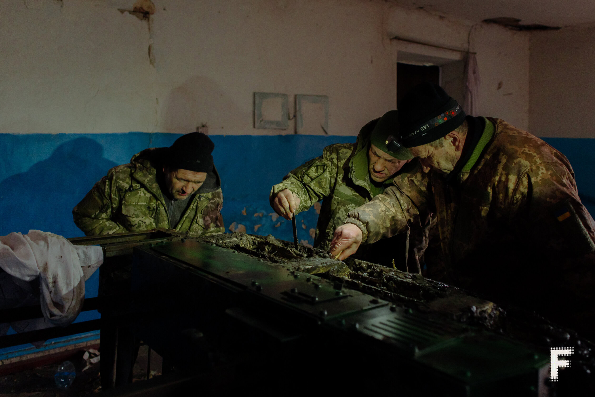 Українські військові в камуфляжі оглядають і ремонтують наземний роботизований пристрій (UGV)