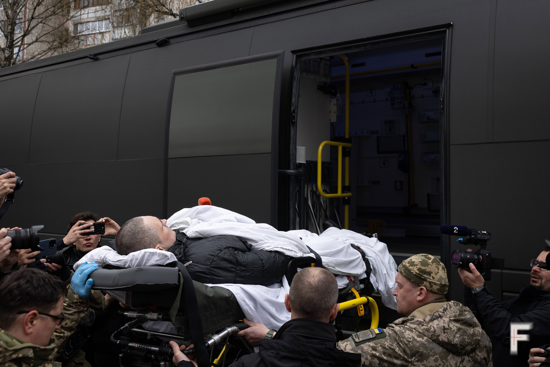 Звільненого військовополоненого виносять на ношах із автобуса, його підтримують військові, Україна, 2026