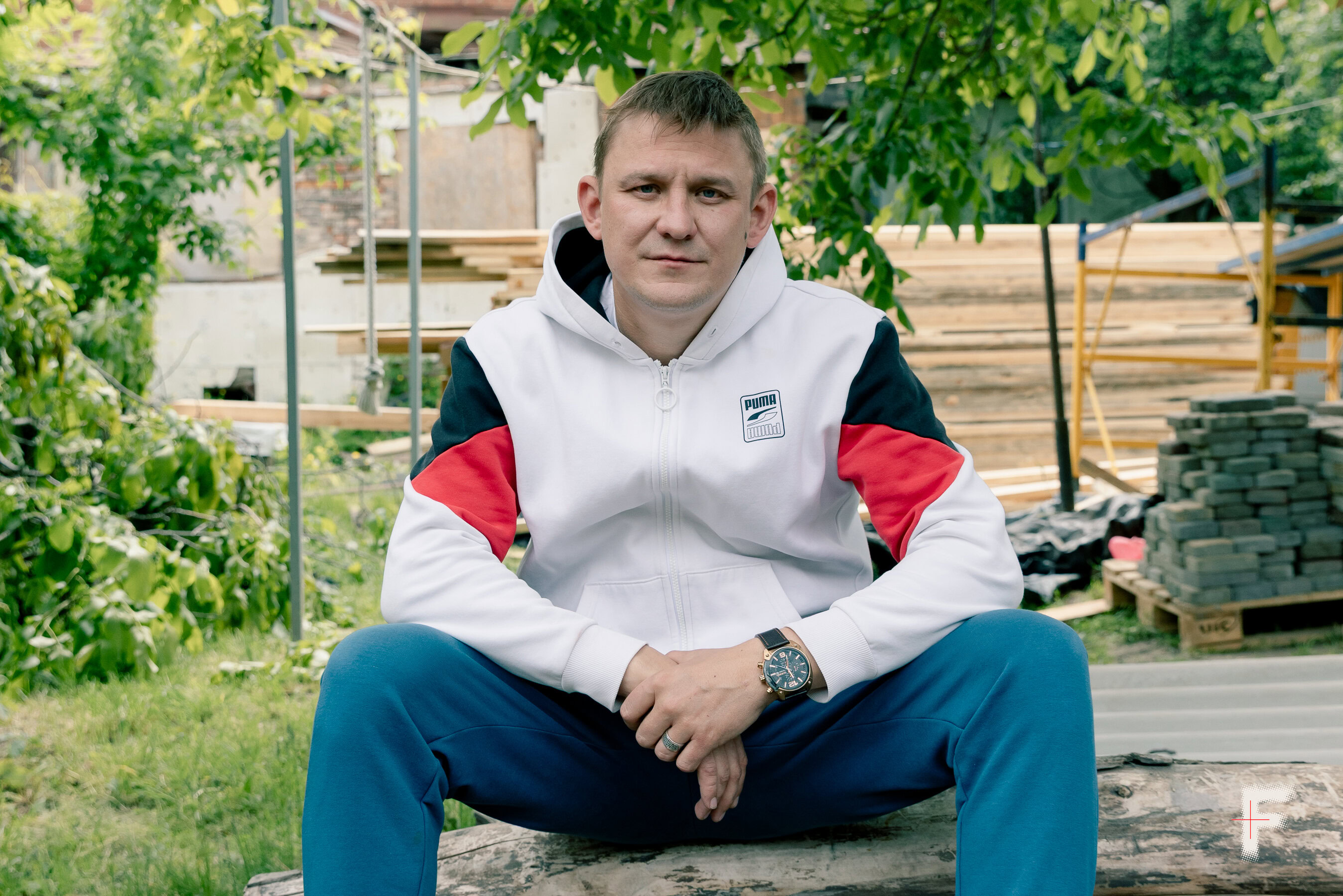 Чоловік у спортивному одязі, який пережив російський полон після окупації, сидить на стовбурі дерева зі схрещеними руками.