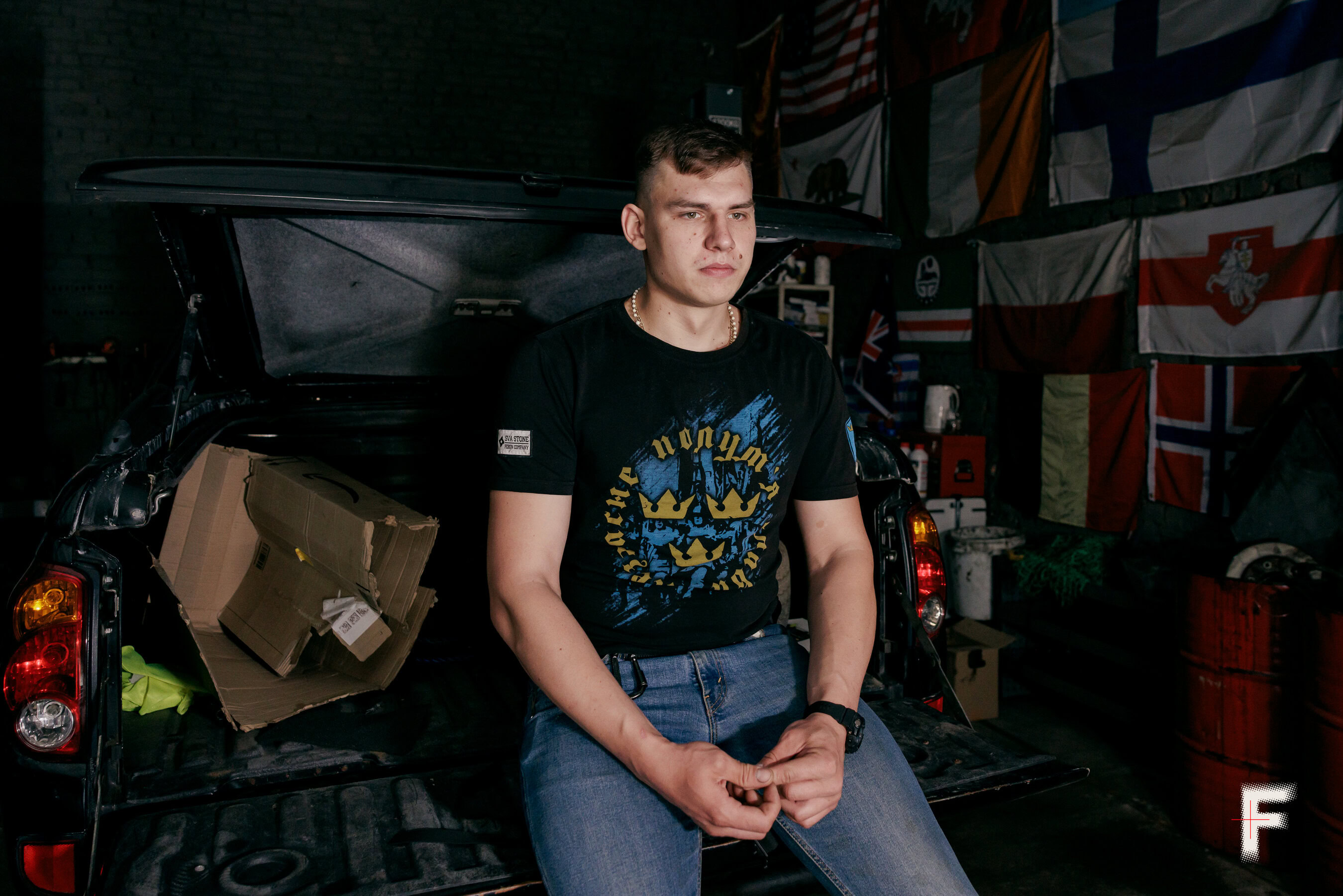 Молодий власник ветеранського гаража сидить на кузові пікапа, який ремонтують.